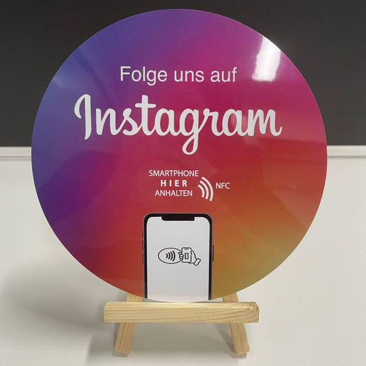 Ein Aufkleber für Schaufenster mit 15cm Durchmesser. Darauf steht FOlge uns auf Instagram "Smartphone hier anhalten NFC". Darauf ist auf ein Handy zu sehen, dass die Menschen sehen, dass sie mit dem Handy anhalten sollen. Sie kommen direkt auf deine Instagram Seite und können einen Einblick in dein Business haben. Schnell und unkompliziert. Der Instagram Schaufenster Aufkleber hat die Farben wie instagram. Lila, pink, orange.